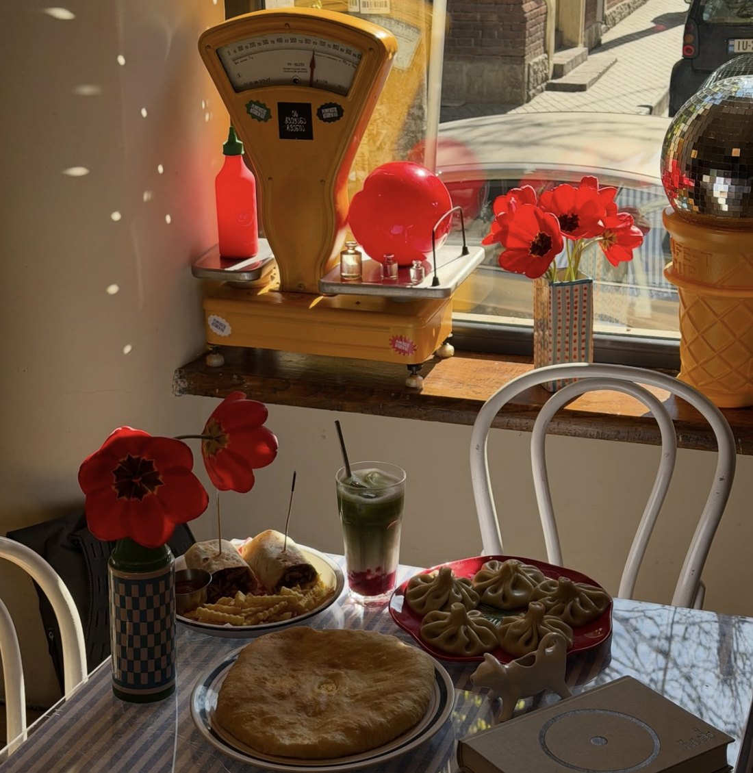 A sunny window table at Plantastic Kitchen with wraps, fries, khinkali, an iced matcha and red tulips